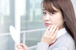 © hikari_stock - 肌やメイクをチェックするために鏡をのぞく女性