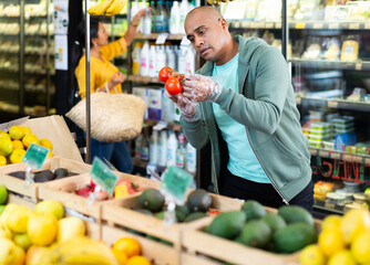 Man shopper chooses ripe tomatoes at grocery supermarket