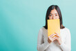 Young beautiful Asian woman hiding behind an open book, Portrait female in glasses is holding and reading a book, studio shot isolated on a blue background, Education concept