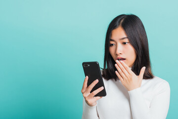 Portrait female anxious scared on the phone seeing bad news, Young beautiful Asian woman surprised shocked with mobile phone close mouth with palm, studio shot isolated on a blue background