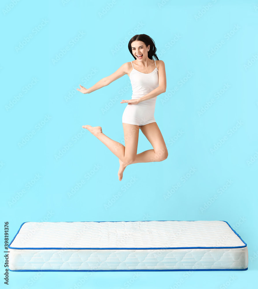 Young woman jumping on mattress against color background