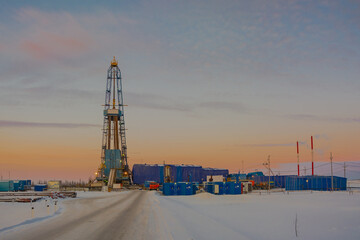 Wall Mural - Winter landscape of a snowy forest tundra with a drilling rig for drilling an oil and gas well in the northern oil and gas field. Polar day sunset. Beautiful bright sky and clouds