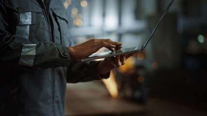 Aufkleber - Close Up on Hands of a Professional Heavy Industry Engineer Wearing Safety Uniform and Using Laptop Computer. African American Industrial Specialist Standing in a Metal Construction Manufacture.