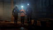 © Gorodenkoff - Three Diverse Multicultural Heavy Industry Engineers and Workers Walk in Dark Steel Factory Using Flashlights on Their Hard Hats. Industrial Contractors Walk Towards the Camera Wearing Safety Unofirm.