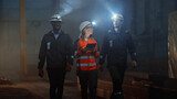 Fototapeta  - Three Diverse Multicultural Heavy Industry Engineers and Workers in Uniform Walk in Dark Steel Factory Using Flashlights on Their Hard Hats. Female Industrial Contractor is Using a Tablet Computer.