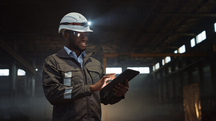 Aufkleber - Professional Heavy Industry Engineer Wearing Safety Uniform and Hard Hat with Flashlight Uses Tablet Computer. Smiling African American Industrial Specialist Standing in a Metal Manufacture Warehouse.