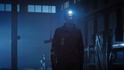 Aufkleber - Professional Heavy Industry Engineer/Worker Wearing Uniform, Flashlight on the Hard Hat in a Steel Factory. Industrial Specialist Walking Towards the Camera in a Dark Metal Construction Manufacture.