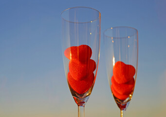 Abstract romantic colorful background. Couple glasses of champagne with red marmalade hearts on blue sky background with copy space, selective focus