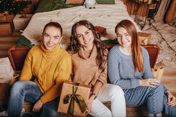 Wall Mural - Three beautiful cheerful happy young girls girlfriend give Christmas gifts on the background of a new year tree at home