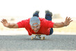 © alex.pin - Uomo settantenne con una polo rossa,  scherza con il suo skateboard stando in una strada di campagna