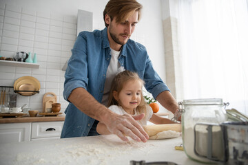 Wall Mural - Caring young Caucasian father and cute little preschooler daughter bake in kitchen at home together