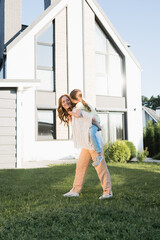 Smiling mother piggybacking daughter near modern house