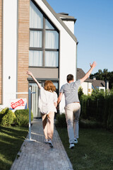 Wall Mural - Back view of couple with hands in air near sign with sold lettering and modern house