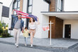 © LIGHTFIELD STUDIOS - Daughter with happy mom and dad holding american flag going forward near sign with sold lettering and house