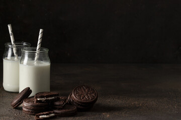 Wall Mural - Sandwich biscuits cookies filling with vanilla cream and two milkj jars on dark background for breakfast concept.