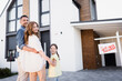 Happy family with daughter hugging and looking at camera near sign with sold lettering and house