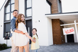 Fototapeta  - Happy family with daughter hugging and looking at camera near sign with sold lettering and house