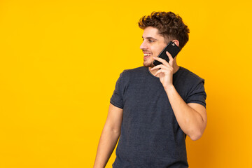 Wall Mural - Young caucasian man isolated background keeping a conversation with the mobile phone with someone