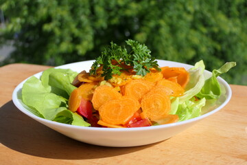 Delicious salad with freshly cut carrots and parsley in a white dish on a wooden plate