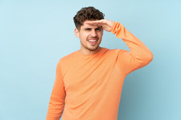 Wall Mural - Caucasian man isolated on blue background looking far away with hand to look something