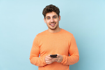 Wall Mural - Caucasian man isolated on blue background sending a message with the mobile