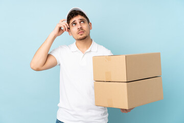 Delivery caucasian man isolated on blue background having doubts and with confuse face expression