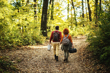 Rear view of young happy couple in love holding hands and walking in nature on a beautiful autumn day. Couple holding picnic equipment.