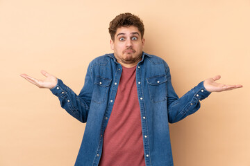 Wall Mural - Caucasian man isolated on beige background having doubts with confuse face expression