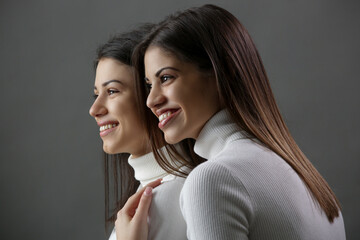 Studio portrait of two brunette girls in classic white turtleneck shirt. Head shot of young beautiful women on grey background.