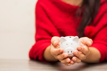 asian women in red shirt insert coin to putting in piggy bank for saving money and investing in future