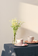 Two Pink Ceramics Cups With Daisy Inside On Vase Round Table In Light Interior.