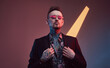 © Fxquadro - Weared with sunglasses stylish and tattooed businessperson with fashionable haircut and beard poses in dark and colourful background with lights.