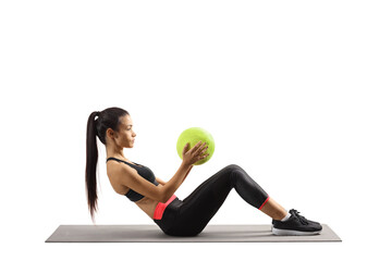 Wall Mural - Full length profile shot of a young woman sitting on a mat and exercising with a ball