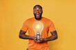 © alphaspirit - Happy afro man holds a lightbulb with hands. Concept of idea and creativity. Orange background