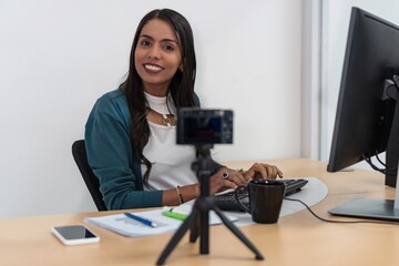 A smiling young Latina working on the computer sitting at a table in the studio