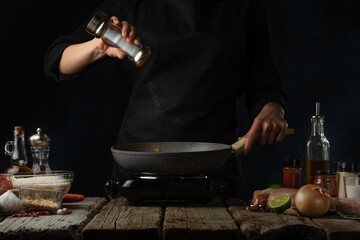 Wall Mural - Professional chef salts frying chicken fillet. Backstage of cooking traditional Indian chicken curry on dark blue background. Frozen motion. Concept cooking process. Frozen motion.