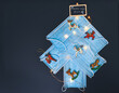 View of a Christmas tree made of blue surgical masks decorated with colorful Christmas ornaments and lights against black chalkboard background. Christmas during pandemic or medical background.