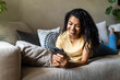 © F8  \ Suport Ukraine - Young happy woman sitting on sofa with mobile phone at home