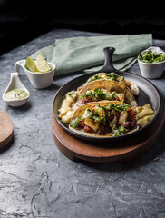 Tacos al pastor accompanied by pineapple, guacamole and spicy sauce served in an iron pan.