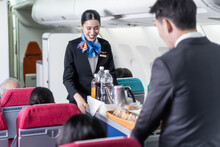 Asian Flight Attendant Serving Food And Drink To Passenger On Airplane