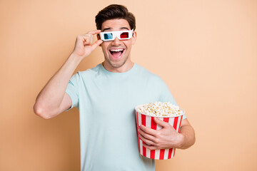 Wall Mural - Portrait of nice cheerful amazed guy eating pop corn watching film touching 3d specs isolated over beige pastel color background