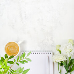 Wall Mural - Cup of coffee, eustoma, pistachio greenery, notepad and pen on concrete background