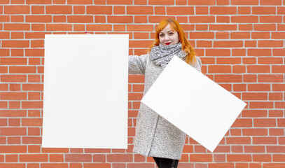 Sticker - Young girl in a white coat stands against brick wall and holds two blank white canvases for painting