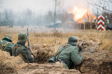 Re-enactors Dressed As German Wehrmacht Infantry Soldiers In World War II Hidden Sitting With Rifles Weapons In An Ambush In Trench