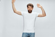 © SHOTPRIME STUDIO - Man with a beard in a white t-shirt with hands raised up jeans gray background