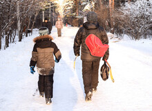 Russia, Chelyabinsk, December 05, 2020: Father And Son Are Walking In The Winter Park For Hockey Training. A Man Carries A Sports Bag And Hockey Sticks. Winter Sport Concept.