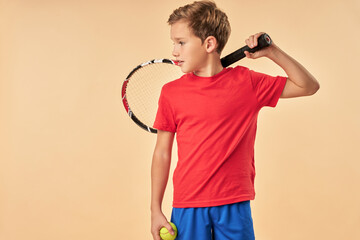 Cute boy tennis player standing against light orange background