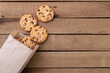 © Odu Mazza - Chocolate chip cookies on a paper bag over a wooden table with copy space