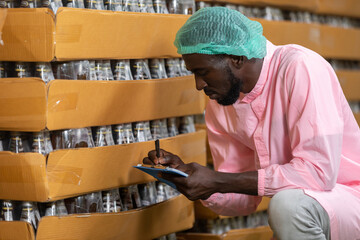 Wall Mural - African male factory worker holding pen and clipboard looking or checking for stocktaking of products in beverage factory