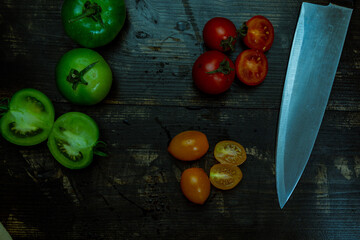 Wall Mural - High angle shot of sliced ripe and unripe tomatoes with knife and napkin on a wooden table